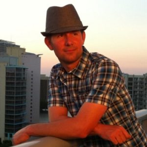 A man in a hat leaning on the railing of a balcony.