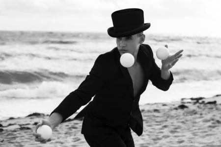 Juggler in suit and hat on beach.