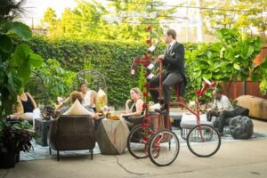 Man on tall bicycle in garden setting.