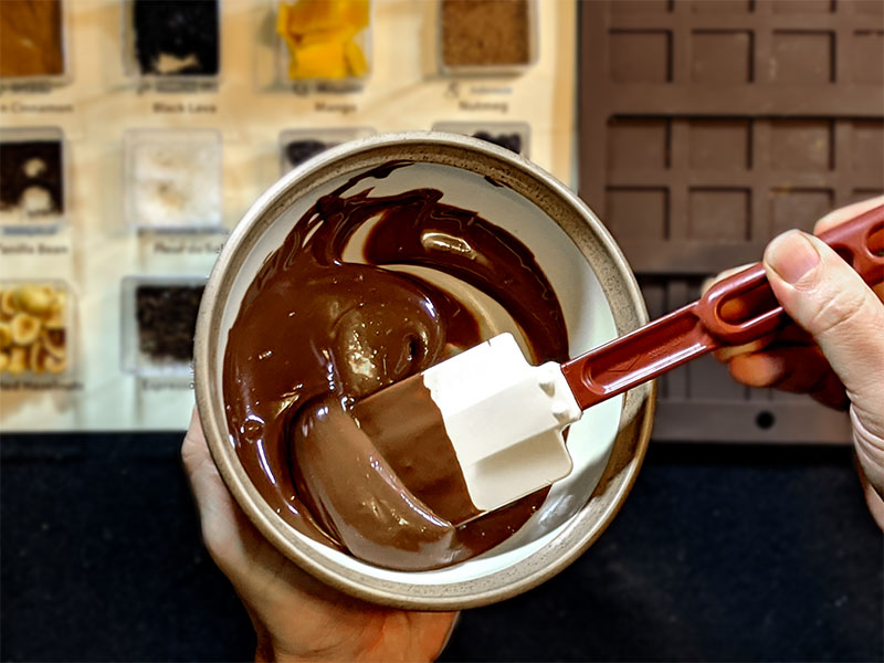 Hands stirring melted chocolate in bowl.
